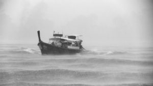 schwarz-weiß Bild, auf dem ein kleines Fischerboot in Wellen und Regen zusahen ist.