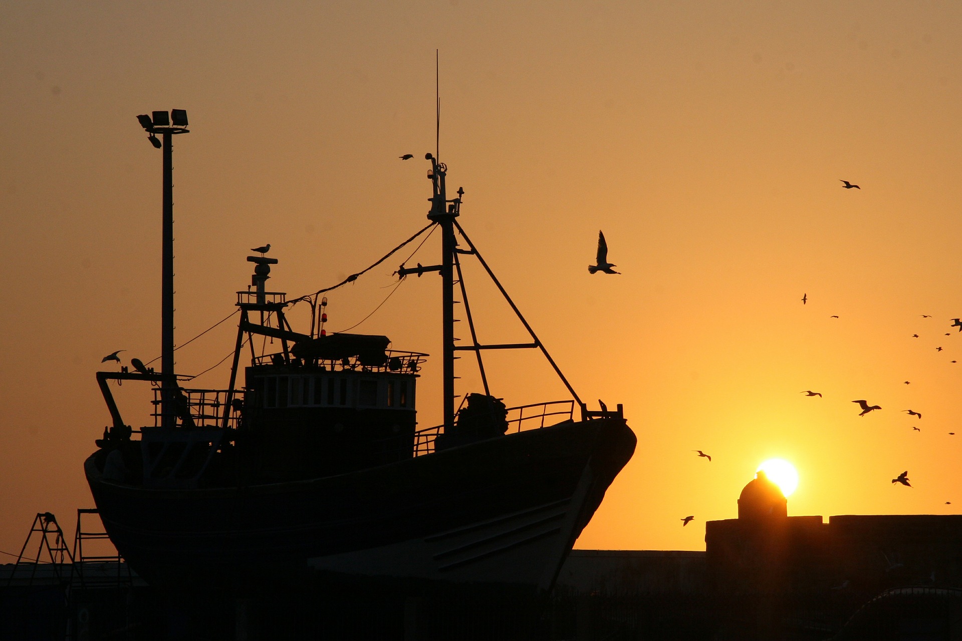 Ein Fischereiboot liegt im Wasser, der Himmel ist orange durch den Sonnenuntergang