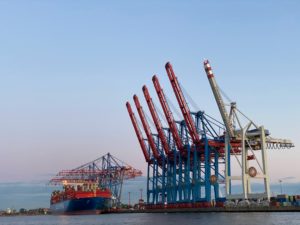Im Hamburger Hafen werden Kräne und ein Frachtschiff vom Sonnenuntergang angestrahlt