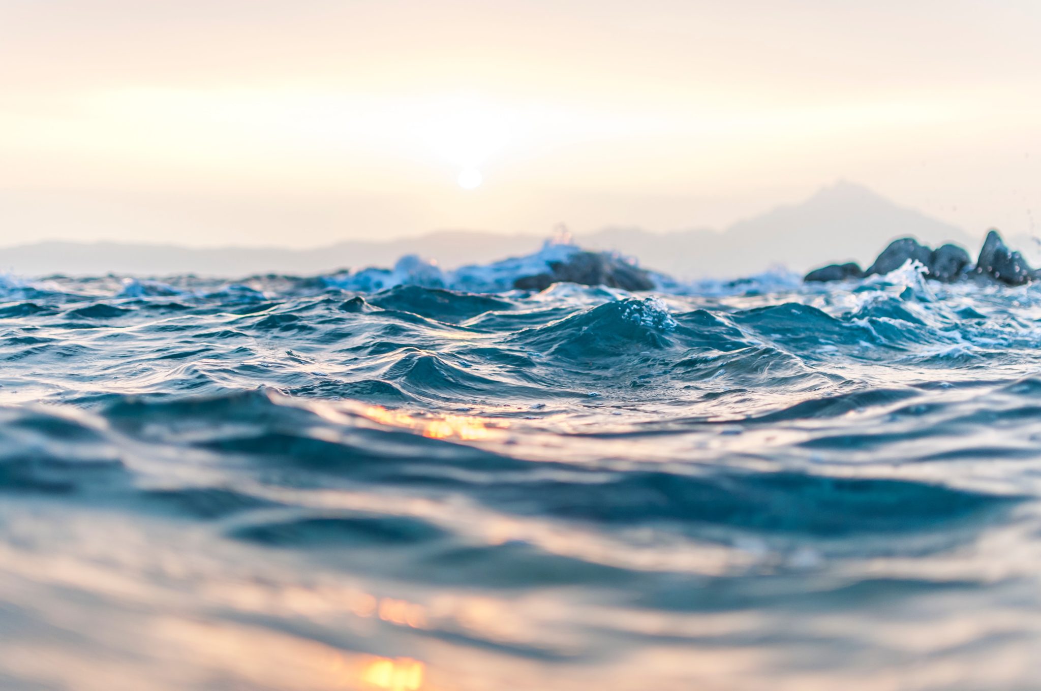 Man blickt direkt an der Meeresoberfläche entlang, die Sonne scheint auf das Wasser und es gibt leichte Wellen