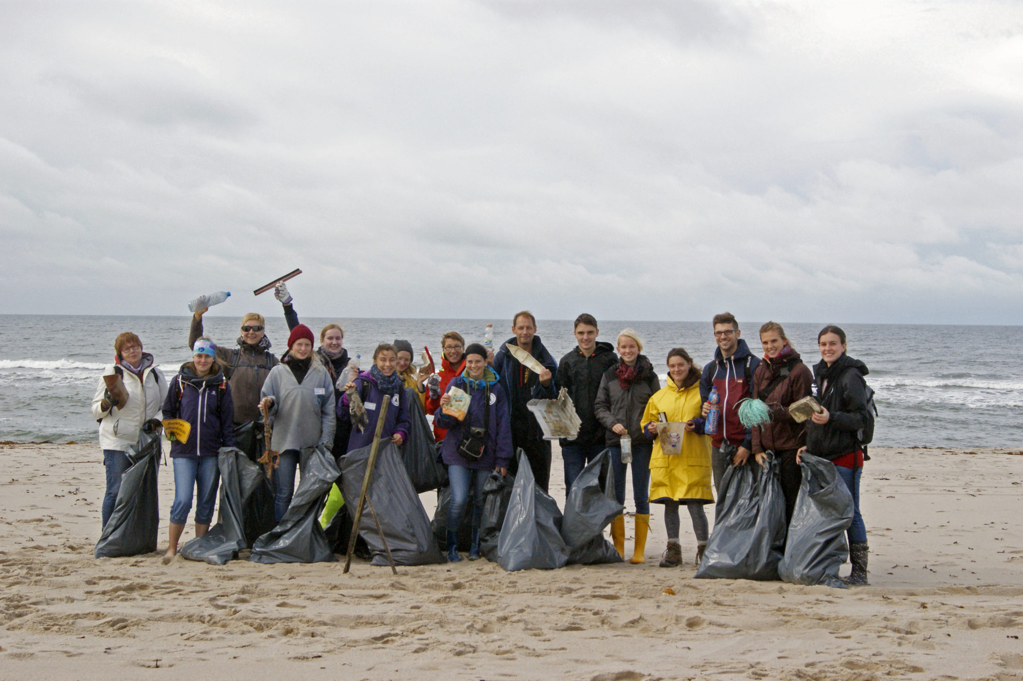 Gruppenfoto mit mehreren Menschen am Strand, die gefüllte Müllsäcke in der Hand halten