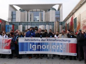 Mehrere Menschen mit zugeklebten Mündern stehen vor dem Kanzleramt und halten ein Plakat von Scientists for Future hoch: "Jahrzente der Klimaforschung ignoriert!"