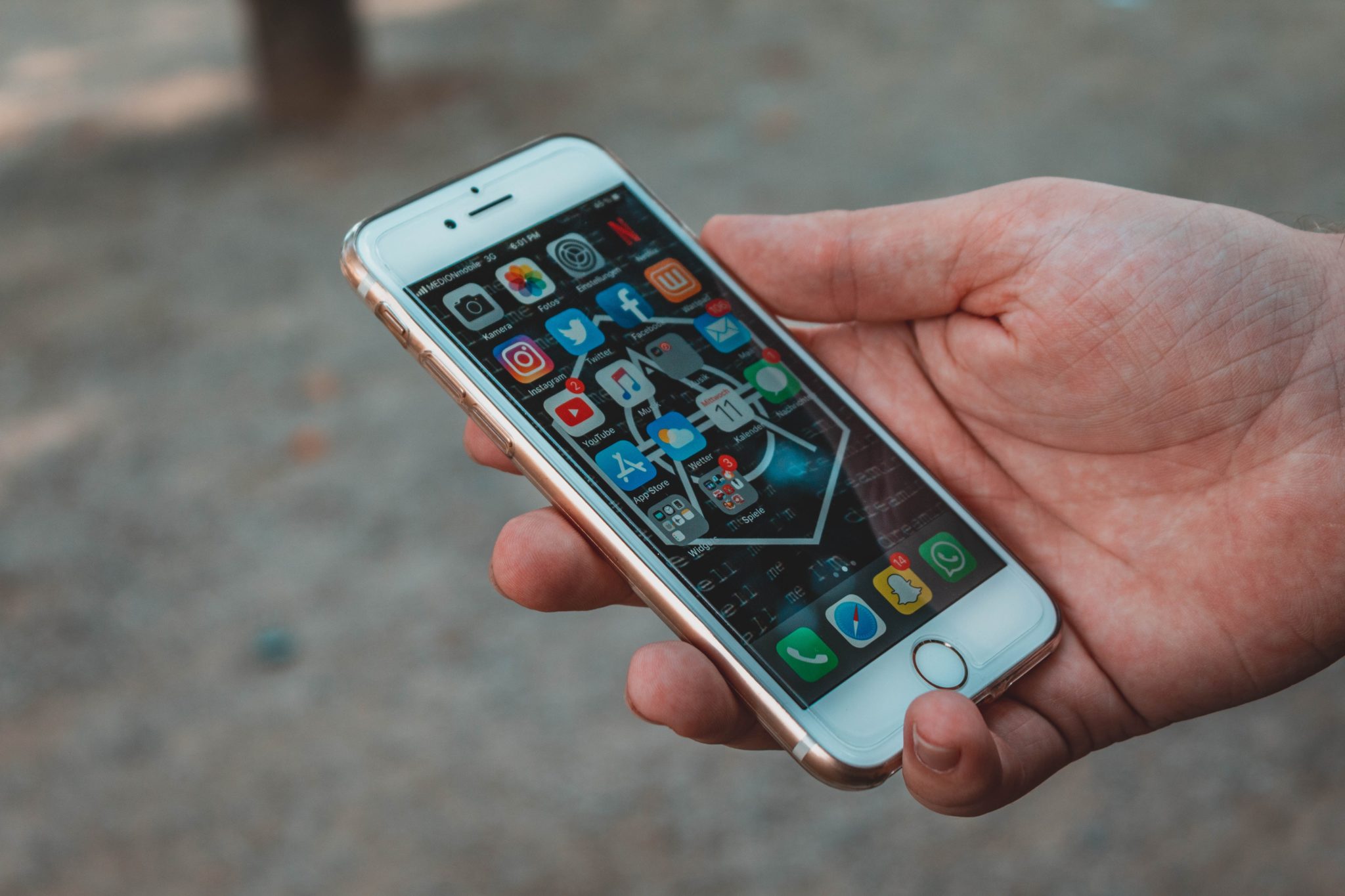 Eine Hand hält ein weißes Iphone, der Bildschirm zeigt viele verschiedene Apps