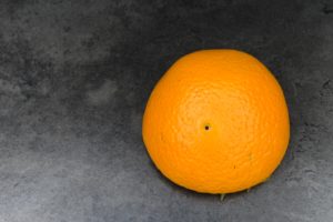 halbe Orange liegt mit dem Fruchtfleisch nach unten auf schwarzer Fläche, nachdem sie gepresst wurde