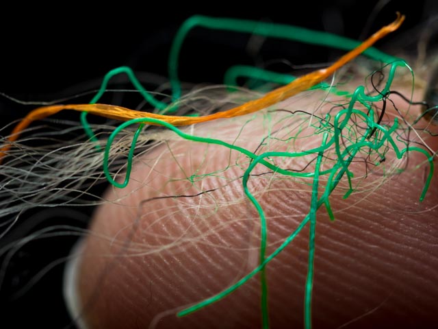 On a finger tip are laying small plastic fibres