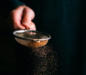 Eine Hand siebt Kakao aus einem kleinen Küchensieb