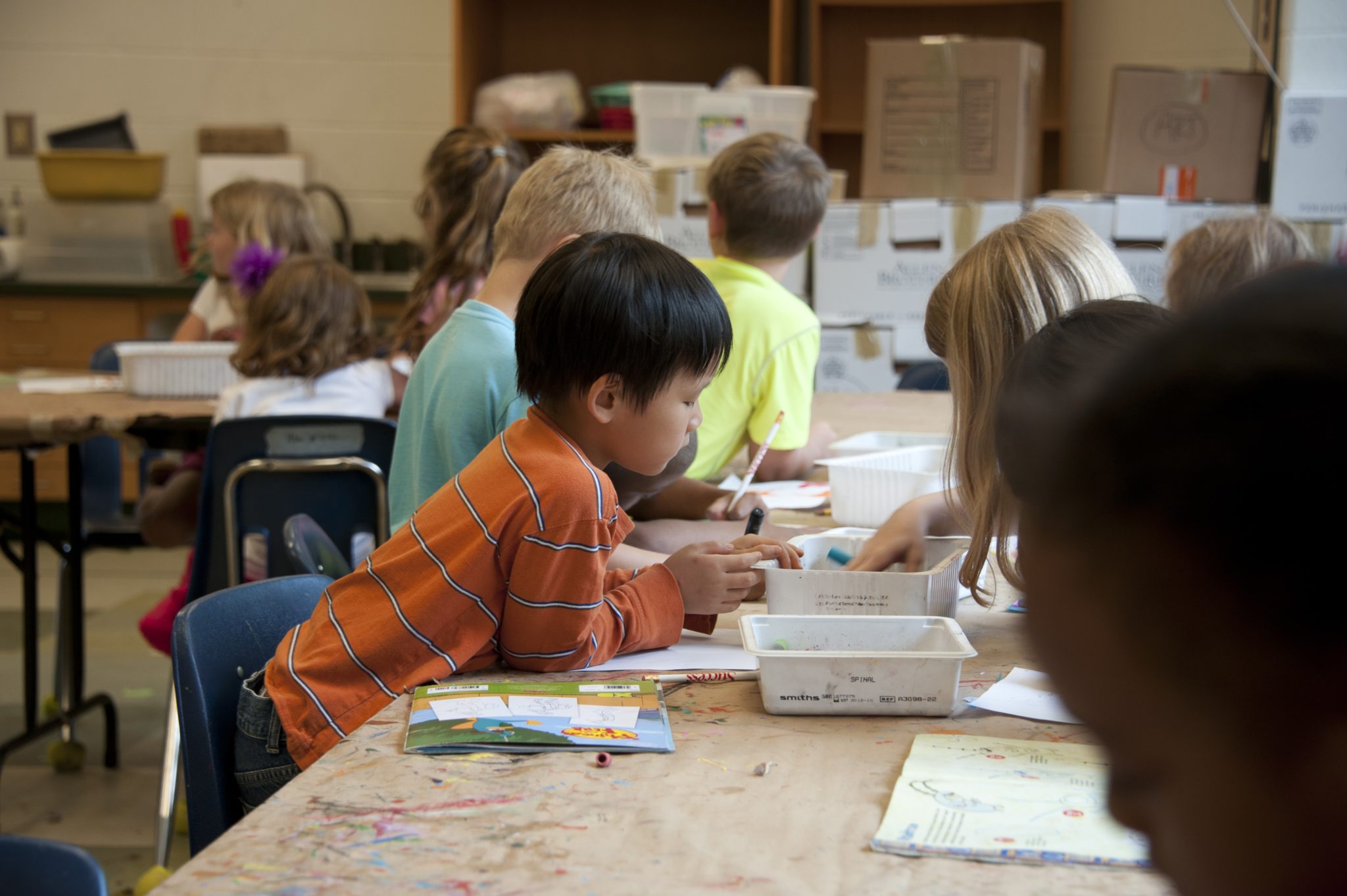 In einem Klassenzimmer beugen sich mehrere Kinder über einen Tisch, auf dem verschiedene Stifte und Papiere liegen.