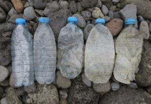 Fünf Einweg-Plastikflaschen liegen nebeneinander an einem Kiesstrand