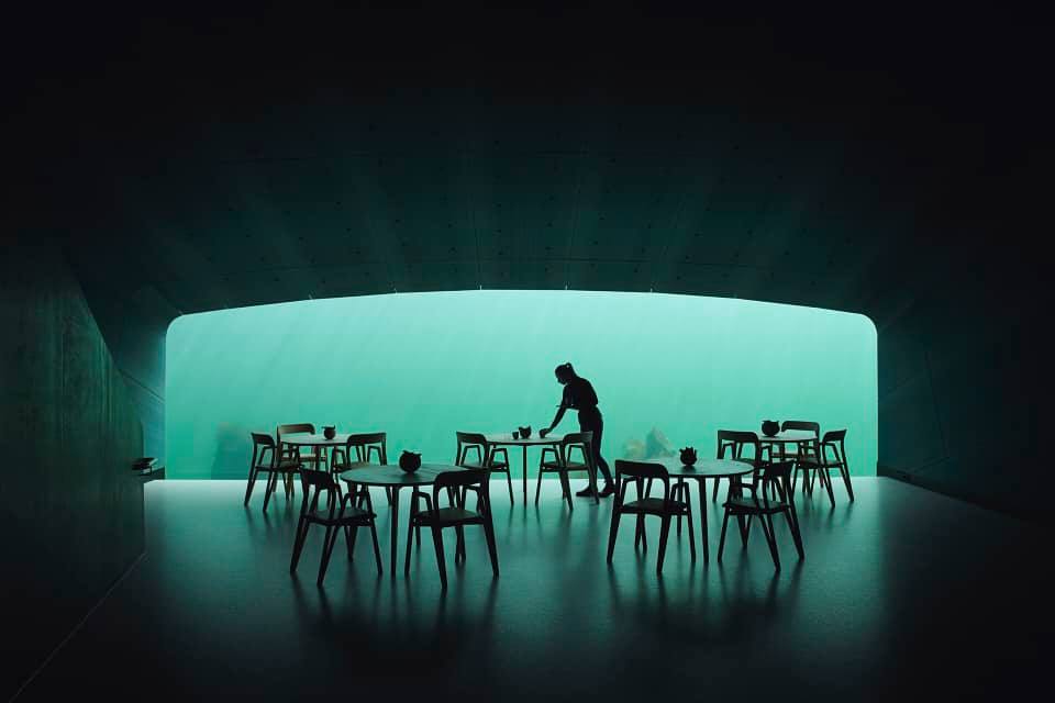 Unterwasserrestaurant mit großer Glasscheibe und Stühlen im Vordergrund.