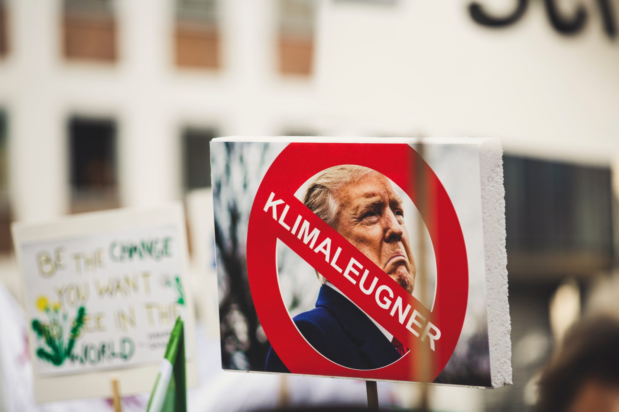 Ein Protestschild, auf dem Trumps Gesicht zu sehen ist, über dem ein rotes Warnschild mit der Schrift "Klimaleugner" gedruckt ist."