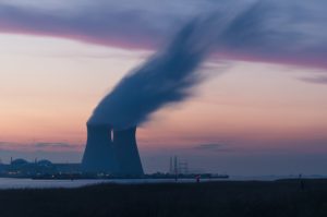 Die Skyline einer Atomkraftanlage mit zwei Atomkraftwerken aus denen Rauch aufsteigt.Es ist Abendstimmung mit Sonnenuntergang.