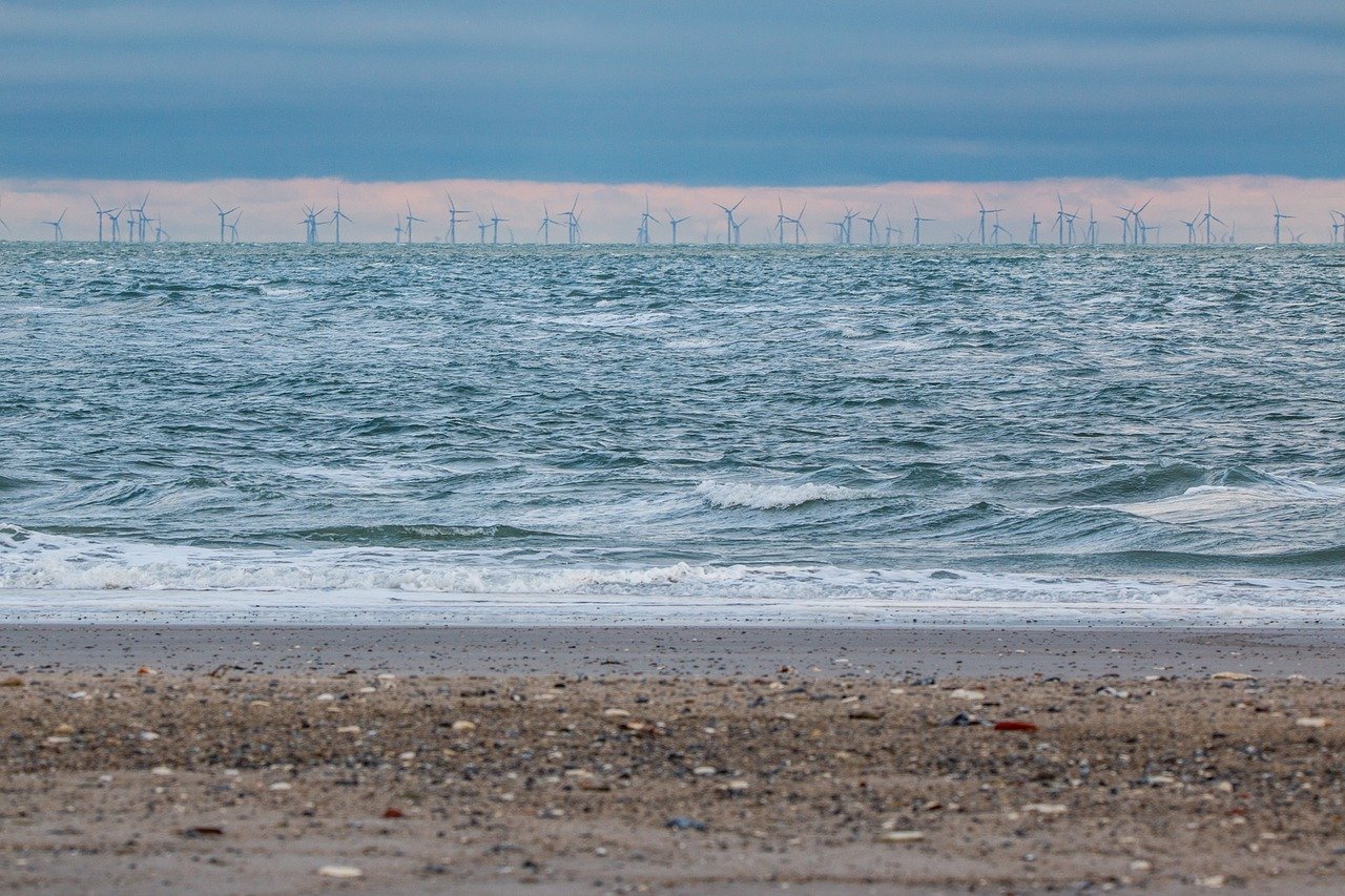Vom Strand aus sieht man in der Ferne auf dem offenen Meer einen großen Offshore-Windpark