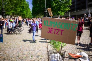 Auf einer Demonstration steht ein Fahrrad mit einem Pappschild auf dem "Klimaschutz jetzt" steht