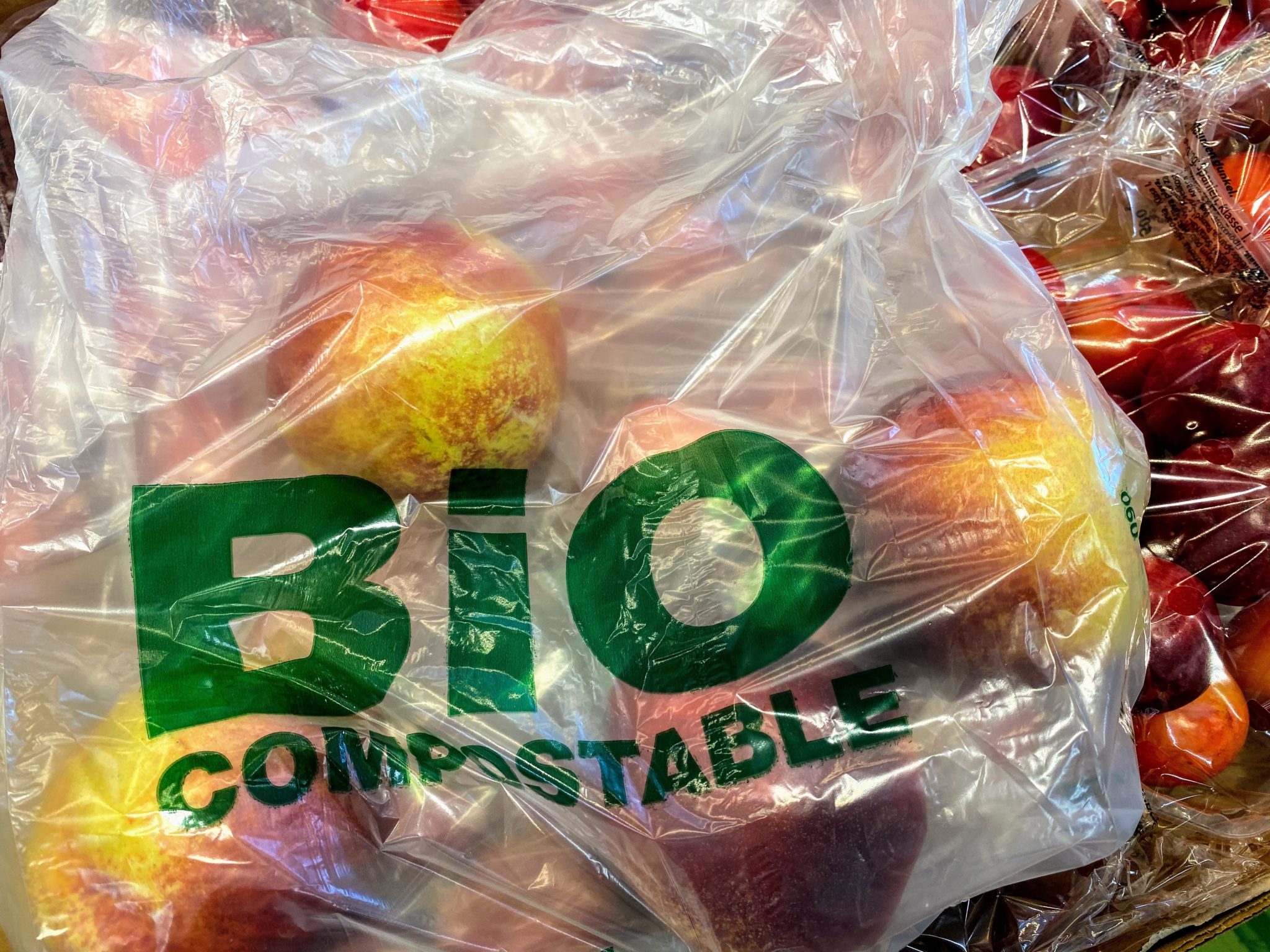 Äpfel sind in einer Türe aus Bioplastik mit dem grünen Aufdruck "BIO compostable" verpackt