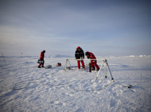 Forschende des Alfred-Wegener Instituts stehen in roten Schneeanzügen auf dem Eis und neben Proben