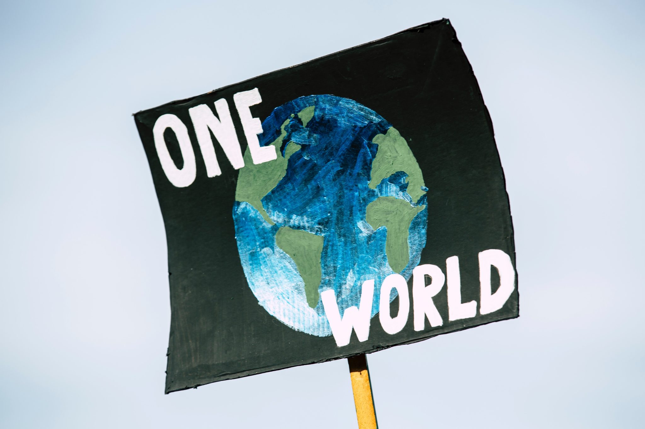 Der 1,5-Grad-Plan: Ein Demonstrationsschild mit der Aufschrift "One World" und einer Erde wird in die Luft gehalten.