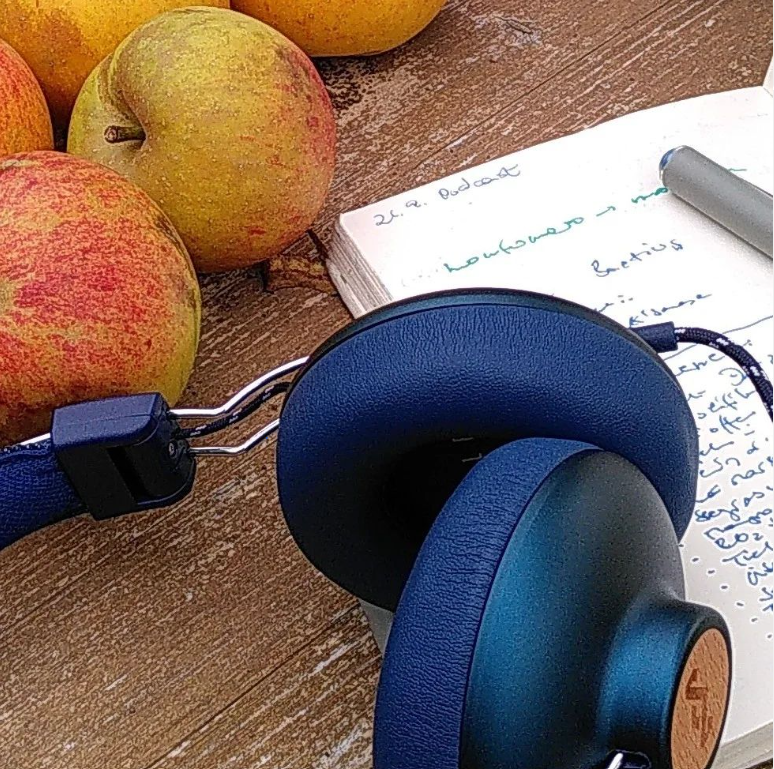 Blaue Kopfhörer liegen neben Äpfeln auf einem Holztisch
