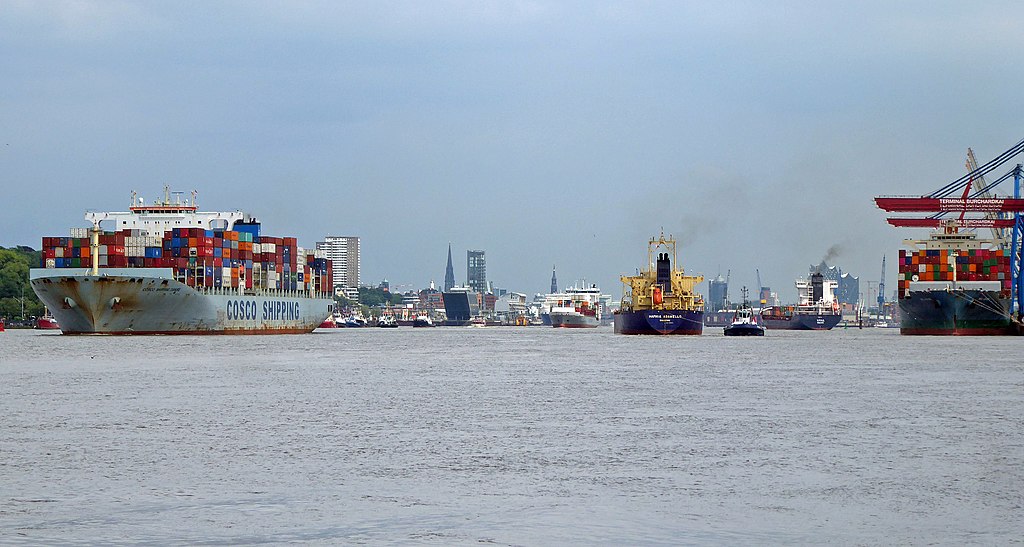 Mehrere Schiffe, eine Fähre und größere Lastenschiffe, fahren nebeneinander auf der Elbe